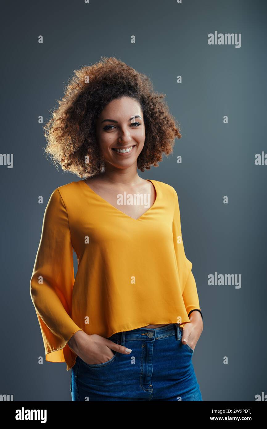 Confiada y elegante, se para con la mano en la cadera, su sonrisa tan atractiva como su sentido de la moda Foto de stock