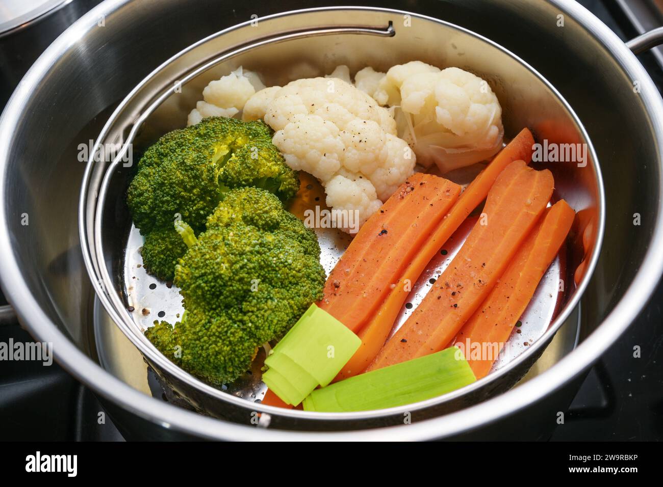 Mezcla de verduras, zanahorias, brócoli y coliflor en una cesta de vapor de alimentos en una olla de acero inoxidable, método de cocción saludable que preserva los minerales, vi Foto de stock