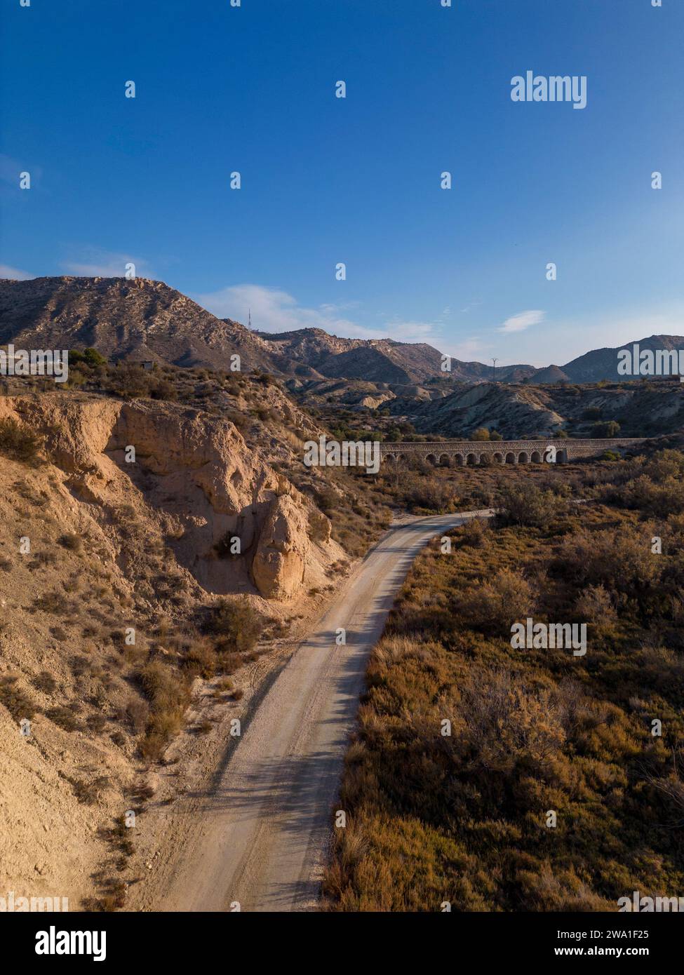 Camino de tierra en paisaje desierto árido con acantilados distantes y luz solar de la mañana, Elche, provincia de Alicante, España - Foto de stock Foto de stock