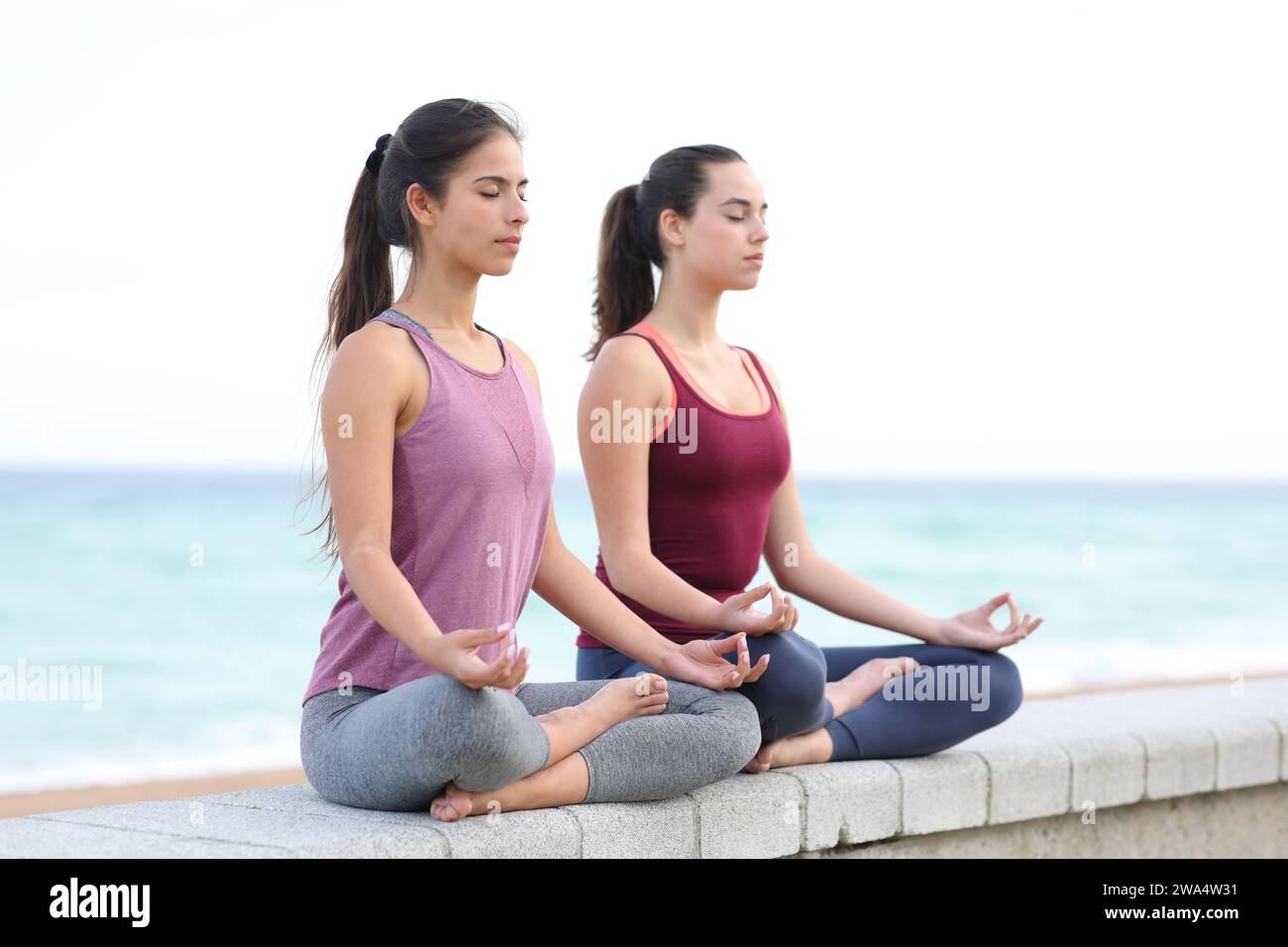 Dos mujeres concentradas haciendo ejercicio de yoga en la playa Foto de stock