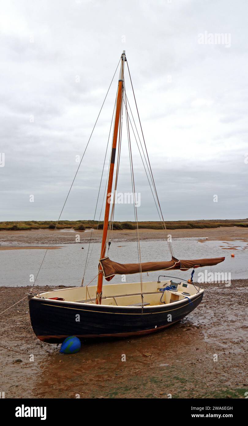 Un bote de vela varado y amarrado en aguas bajas en la costa norte de Norfolk en Burnham Overy Staithe, Norfolk, Inglaterra, Reino Unido. Foto de stock