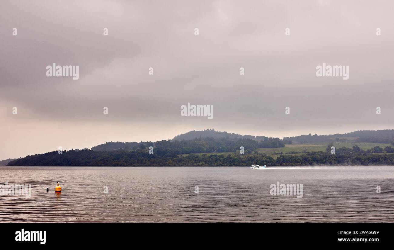 En la distancia, en una mañana de septiembre fría y brumosa, un hidroavión turístico despega del lago Lomond en un viaje turístico. Escocia Foto de stock