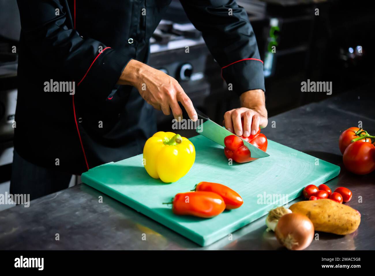 El chef corta meticulosamente las verduras frescas en una tabla de cortar para la preparación de la comida Foto de stock
