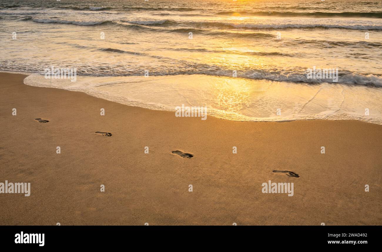 Huellas en la playa de arena al atardecer Foto de stock