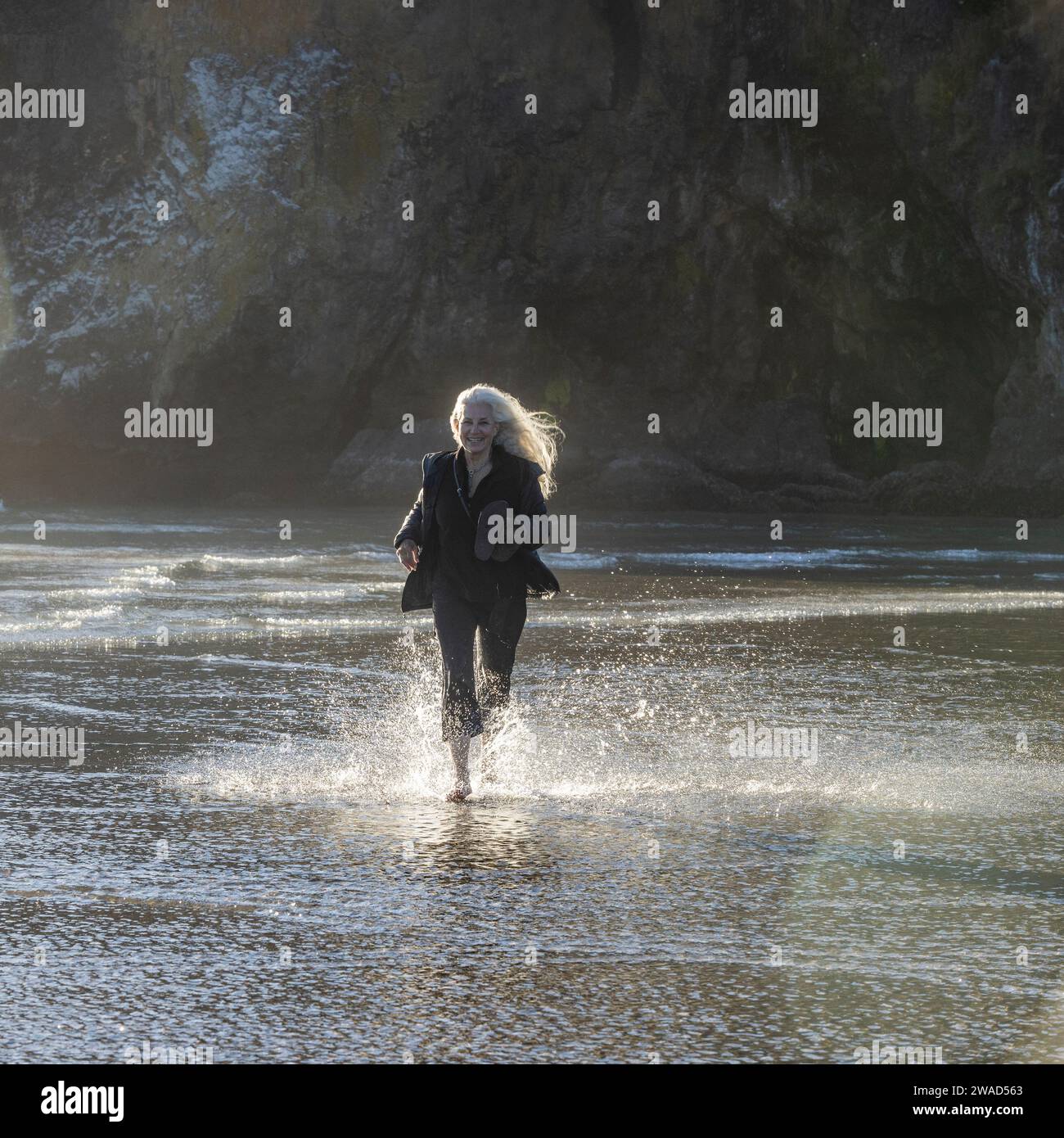 Estados Unidos, Oregon, Newport, mujer corriendo en la playa de arena y salpicando agua Foto de stock