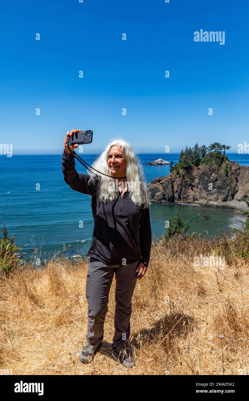 EE.UU., Oregon, Brookings, Mujer mayor tomando selfie con paisaje costero en el fondo Foto de stock