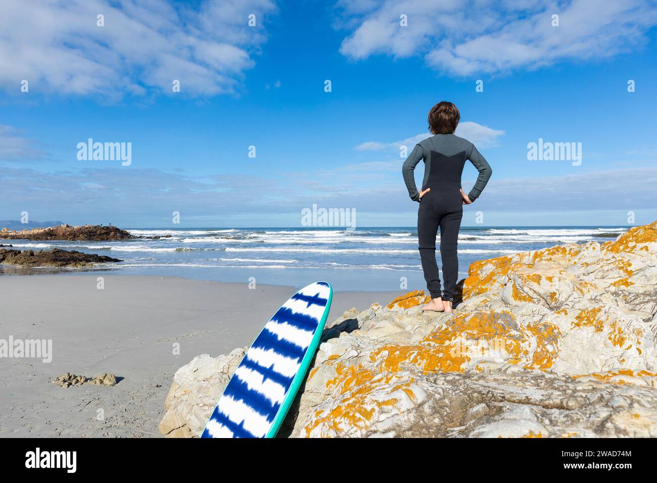 Muchacho (10-11) con el tablero del cuerpo de pie en la playa de Voelklip Foto de stock