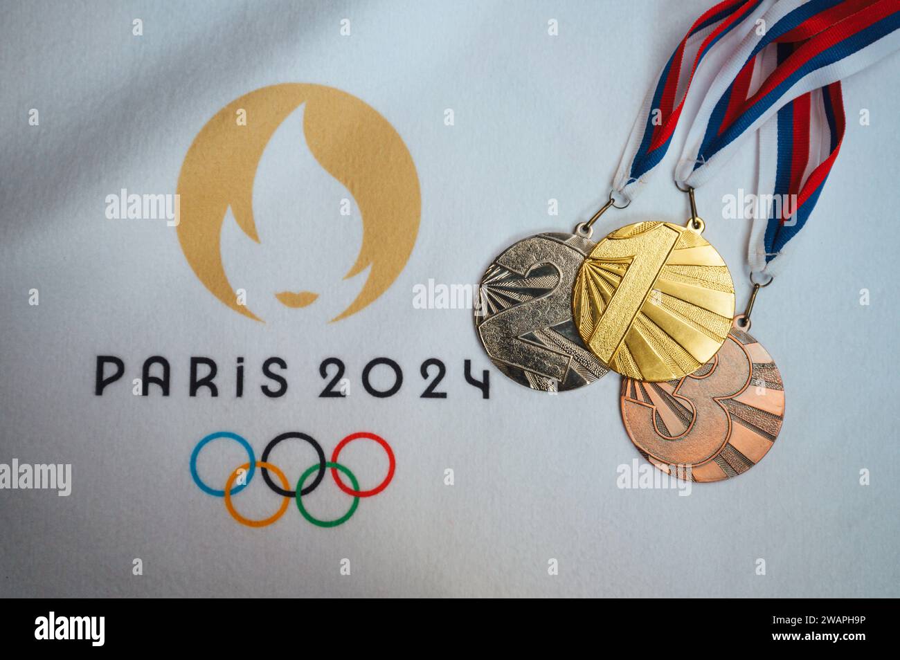 PARÍS, FRANCIA, 4 DE ENERO. 2024: Un destello de la victoria: Medallas de oro, plata y bronce arregladas en manta blanca, logotipo de los Juegos Olímpicos de París 2024 incluido Foto de stock