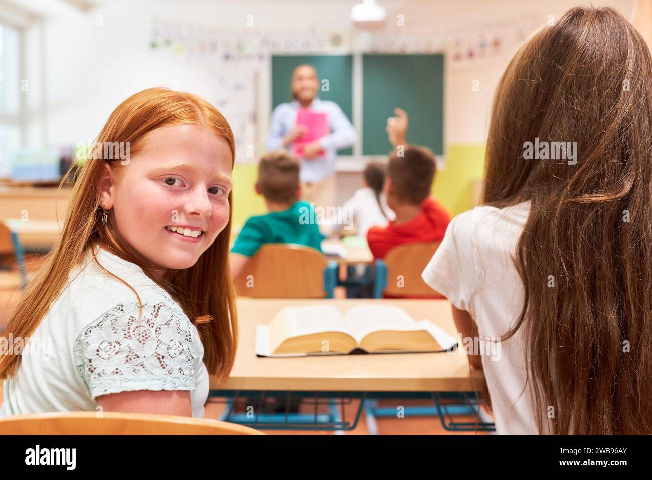 Retrato de la vista lateral de la colegiala sonriente que se sienta con su compañero de clase en la escuela Foto de stock