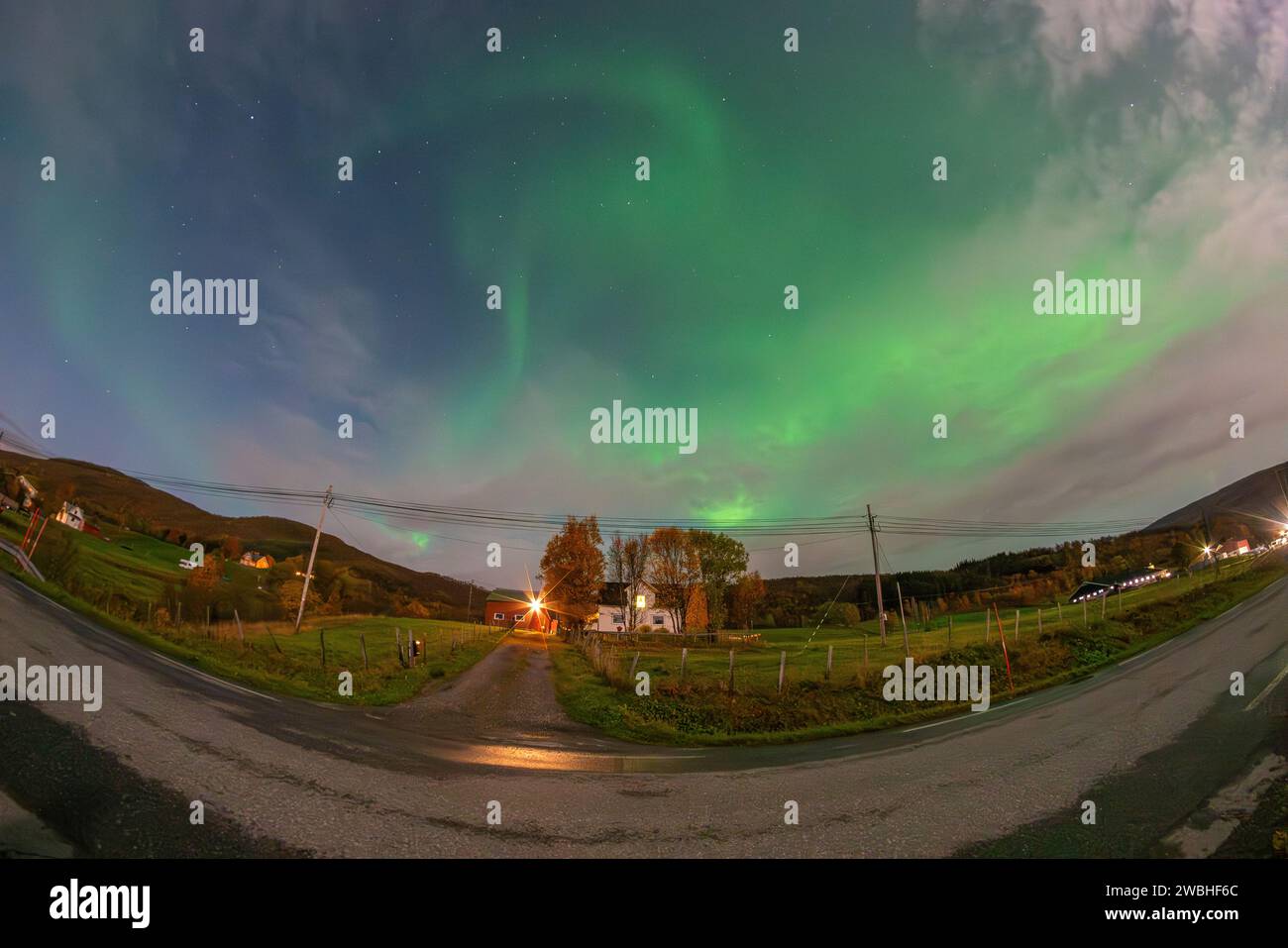 Hermosas luces verdes del norte sobre un fiordo y una casa en la isla de Kvaloya cerca de Tromsø. bailando luces polares sobre una montaña, aurora boreal Foto de stock
