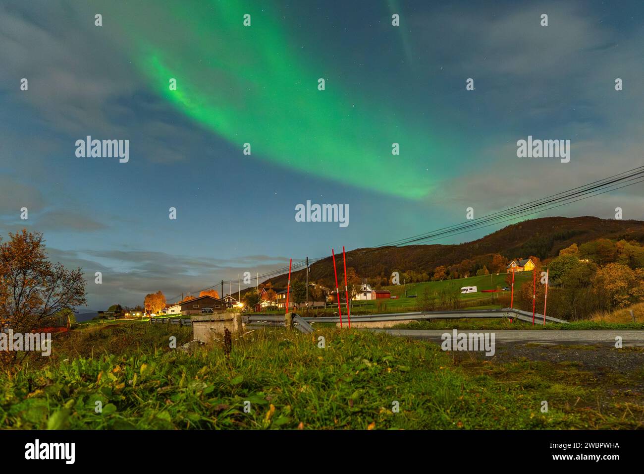Hermosas luces verdes del norte sobre un fiordo y una casa en la isla de Kvaloya cerca de Tromsø. bailando luces polares sobre una montaña, aurora boreal Foto de stock
