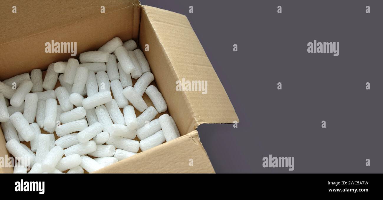 Caja de embalaje de cartón abierta con chips de embalaje de poliestireno blanco. Fondo gris monocromo. Copiar espacio Foto de stock