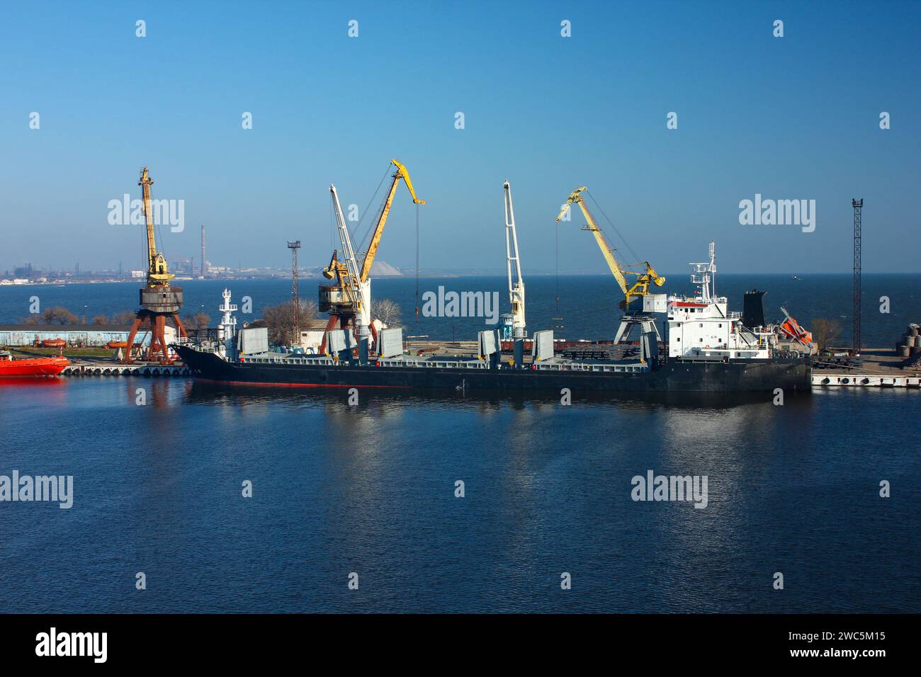 Carga de buques de carga en el muelle con múltiples grúas. Proceso de transbordo industrial en un puerto marítimo. Contenedores en movimiento, operación logística bajo Foto de stock