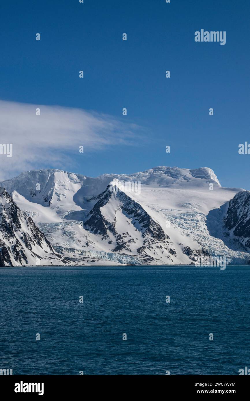 La costa rocosa de la Isla Elefante y los altos picos nevados, el glaciar del Monte Elder que se extiende hacia abajo hacia el océano, empinado y escarpado, Foto de stock
