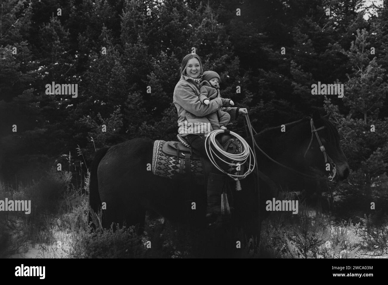 Mamá sostiene al bebé, montando a caballo con alegría juntos Foto de stock