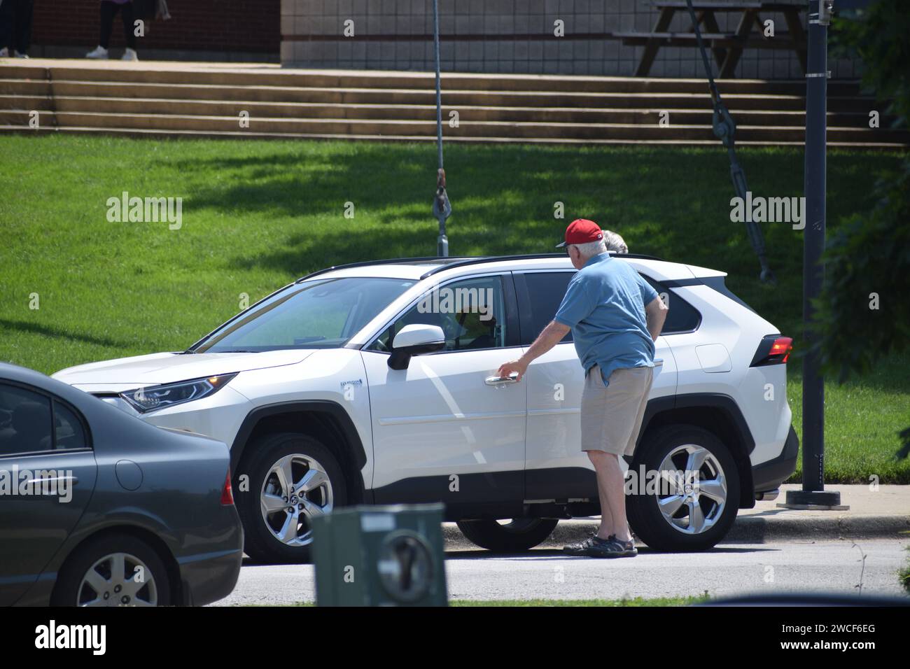 Hombre mayor con una gorra de béisbol roja entrando en su SUV blanco estacionado - Mayo 2023 Foto de stock