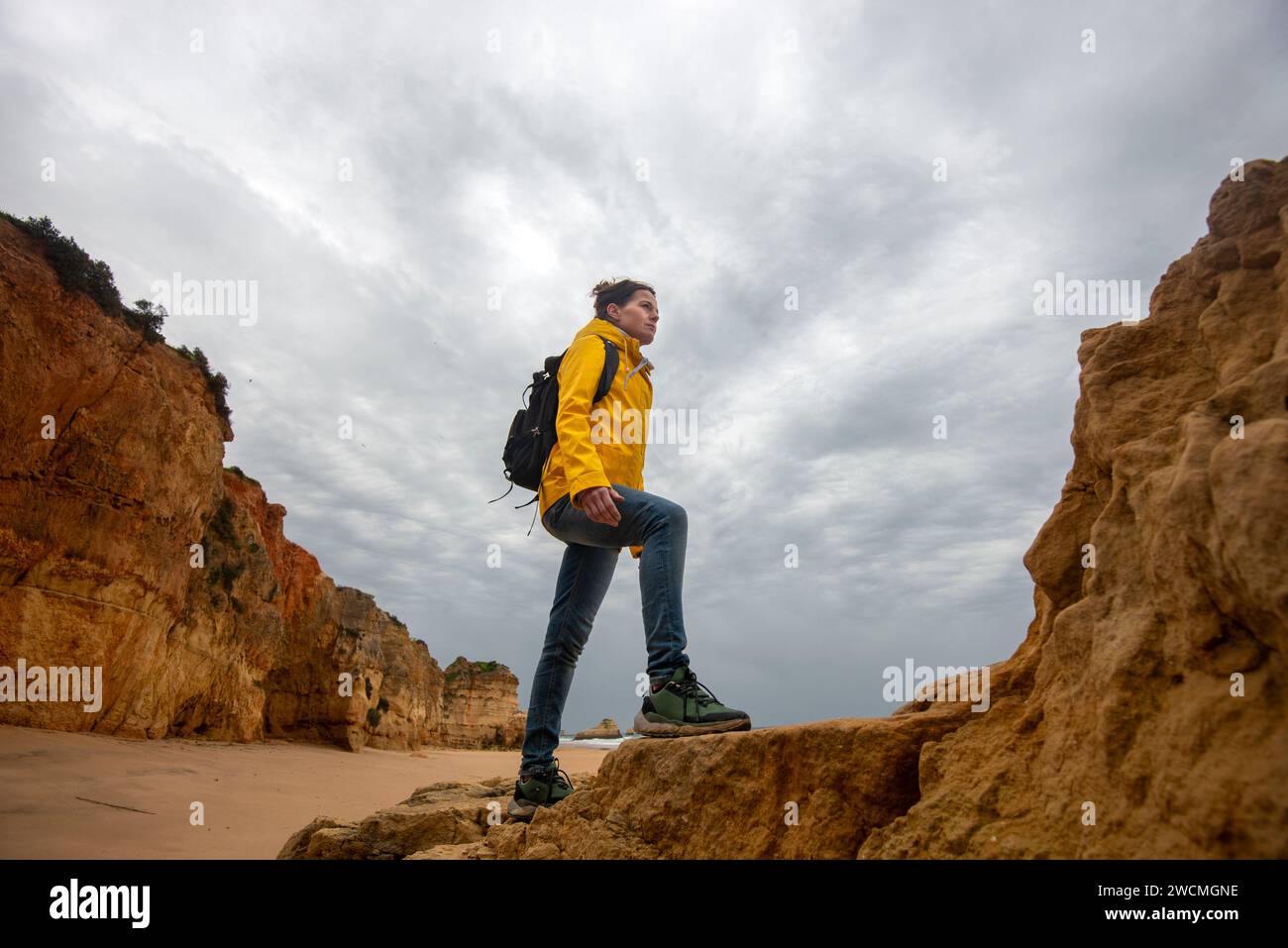 caminante adulto medio caminando sobre rocas y mirando la vista costera en el día sombrío Foto de stock