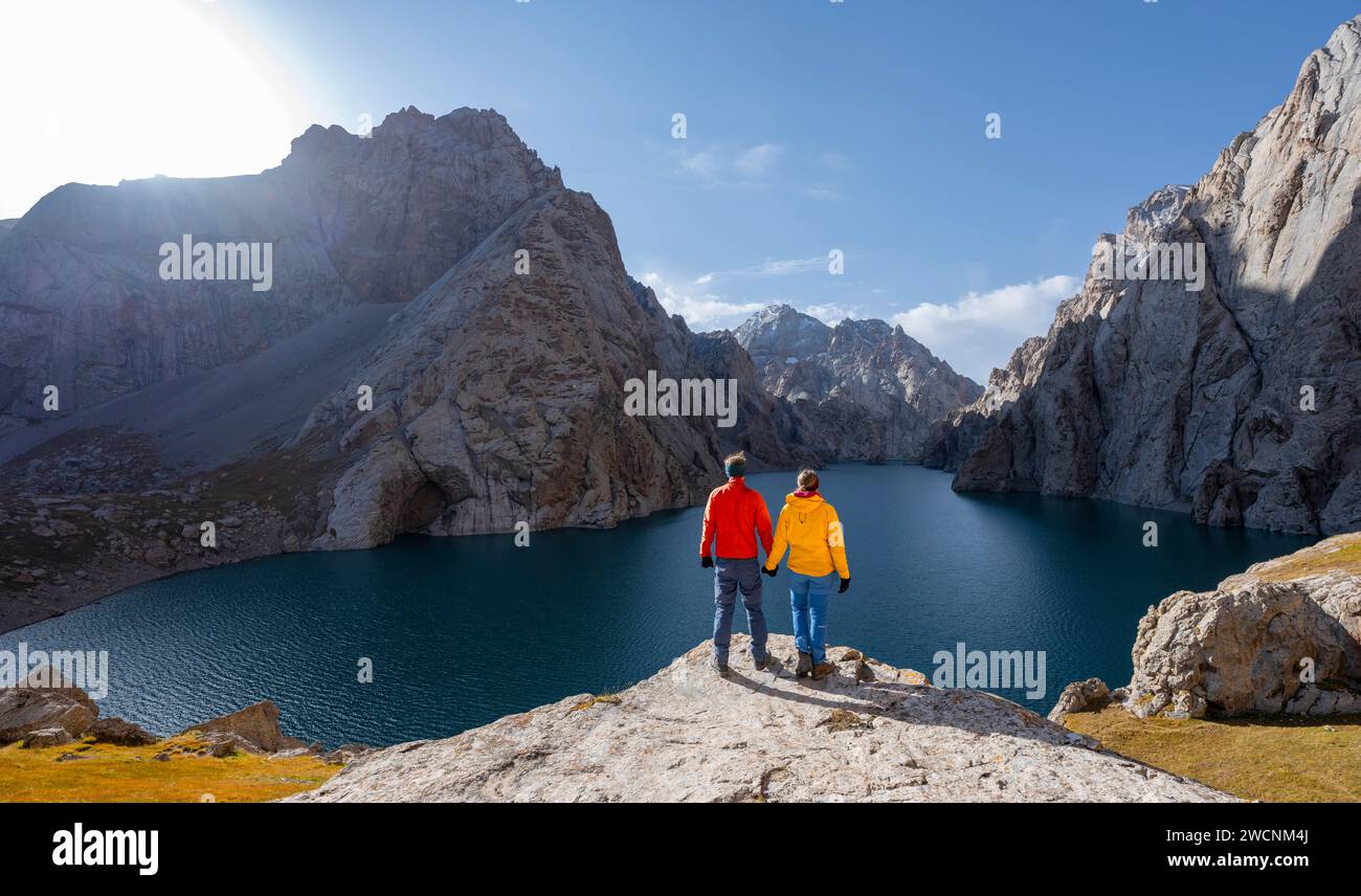 Pareja en el lago de montaña azul entre picos rocosos empinados de las montañas, el lago Kol Suu, las montañas de Sary Beles, la provincia de Naryn, Kirguistán Foto de stock