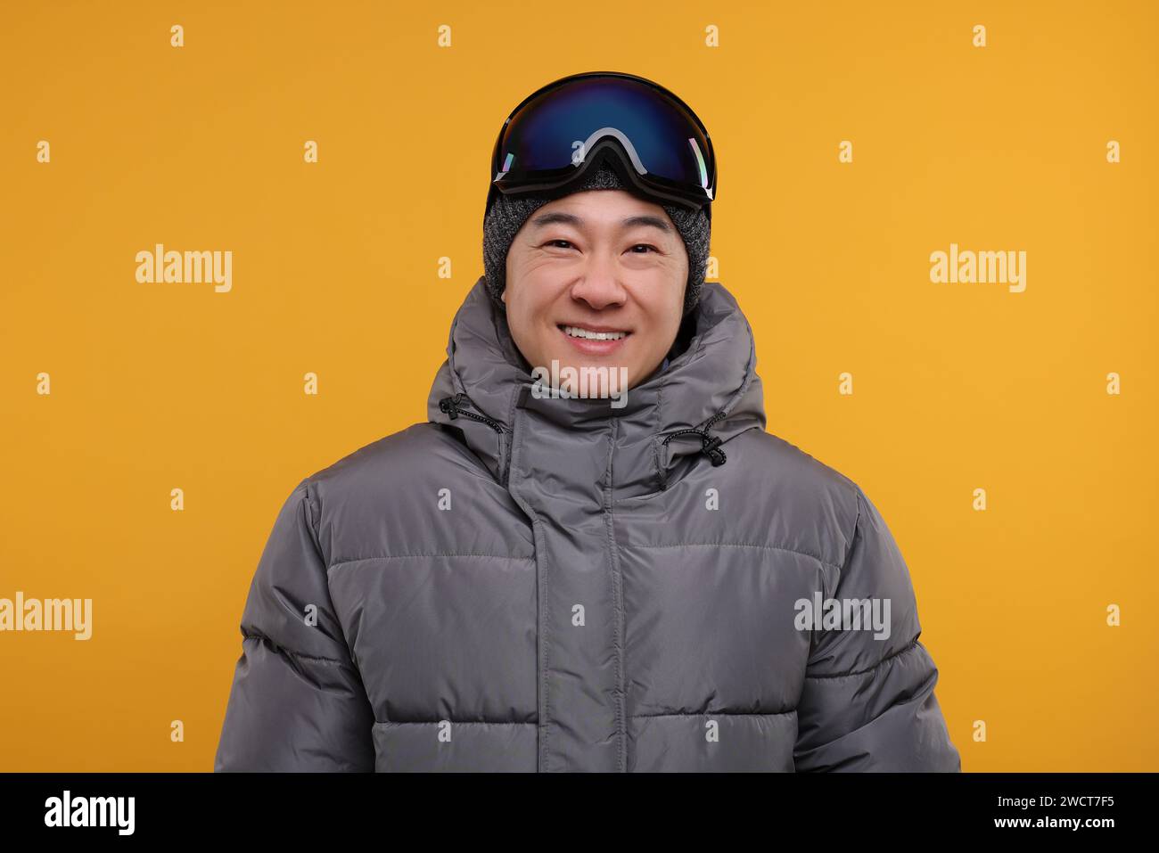 Deportes de invierno. Hombre feliz con gafas de esquí sobre fondo naranja Foto de stock