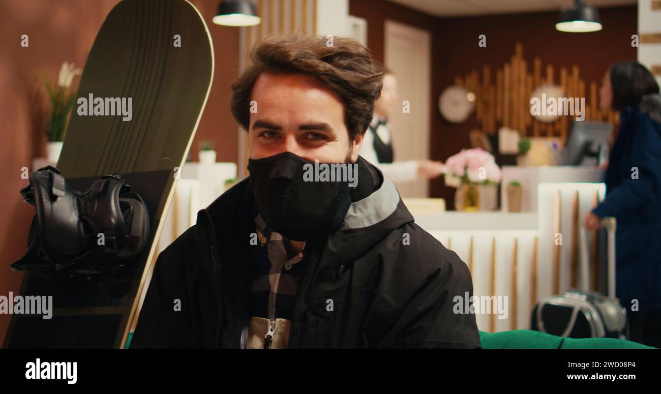 Hombre musculoso llega al complejo de esquí para practicar deportes de invierno con equipo, con traje y casco adecuados. Antes de bajar las pistas para realizar actividades deportivas intensas, los adultos jóvenes se relajan en el hotel. Foto de stock