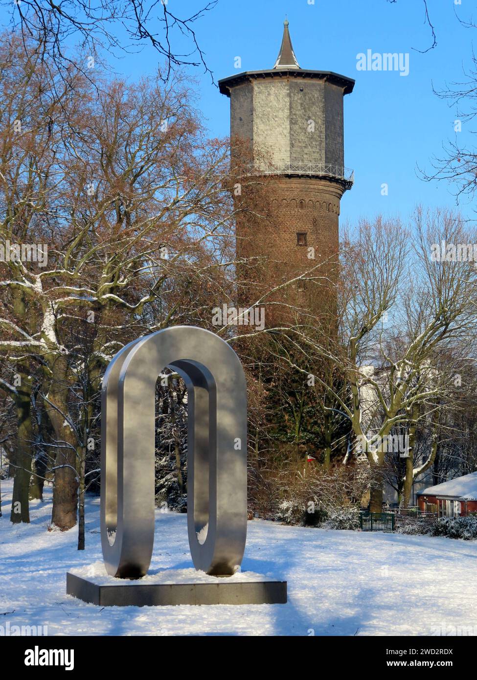 Blick auf die Enndlosschleife von Josef Neuhaus - Ver más detalles sobre la historia de la historia de la historia de Wasserturm am Rand des Stadtparks Winter Schnee Eis histor. Gebaeude und Edelstahlplastik *** Vista del bucle Enndlos por Josef Neuhaus En el fondo se encuentra la histórica torre de agua en el borde del parque de la ciudad Invierno Nieve Hielo edificio histórico y escultura de acero inoxidable Foto de stock