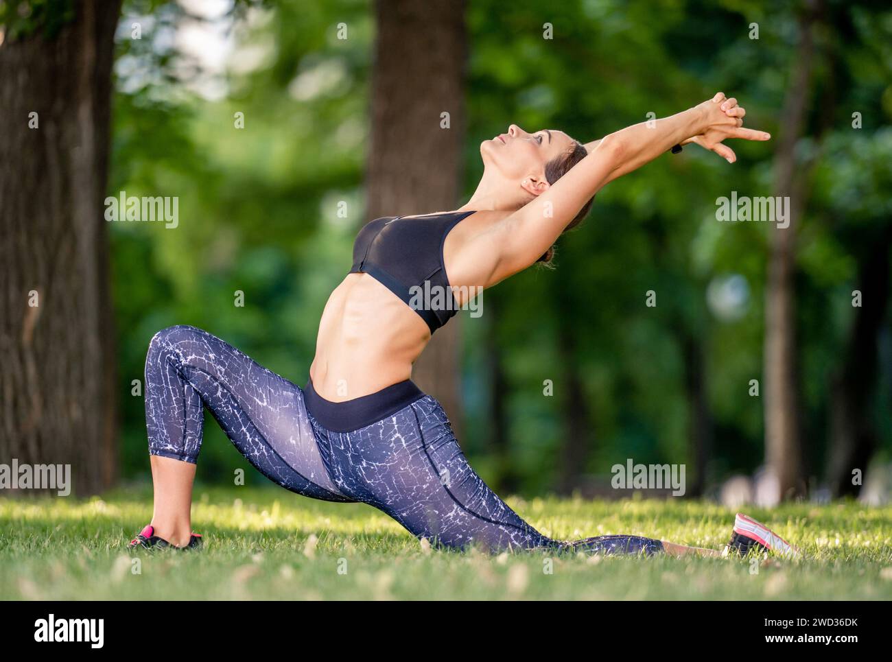 Chica bonita durante el entrenamiento de la mañana de yoga en la naturaleza de pie en pose y estirando sus les y la espalda. Mujer deportiva que hace ejercicio al aire libre en verano Foto de stock