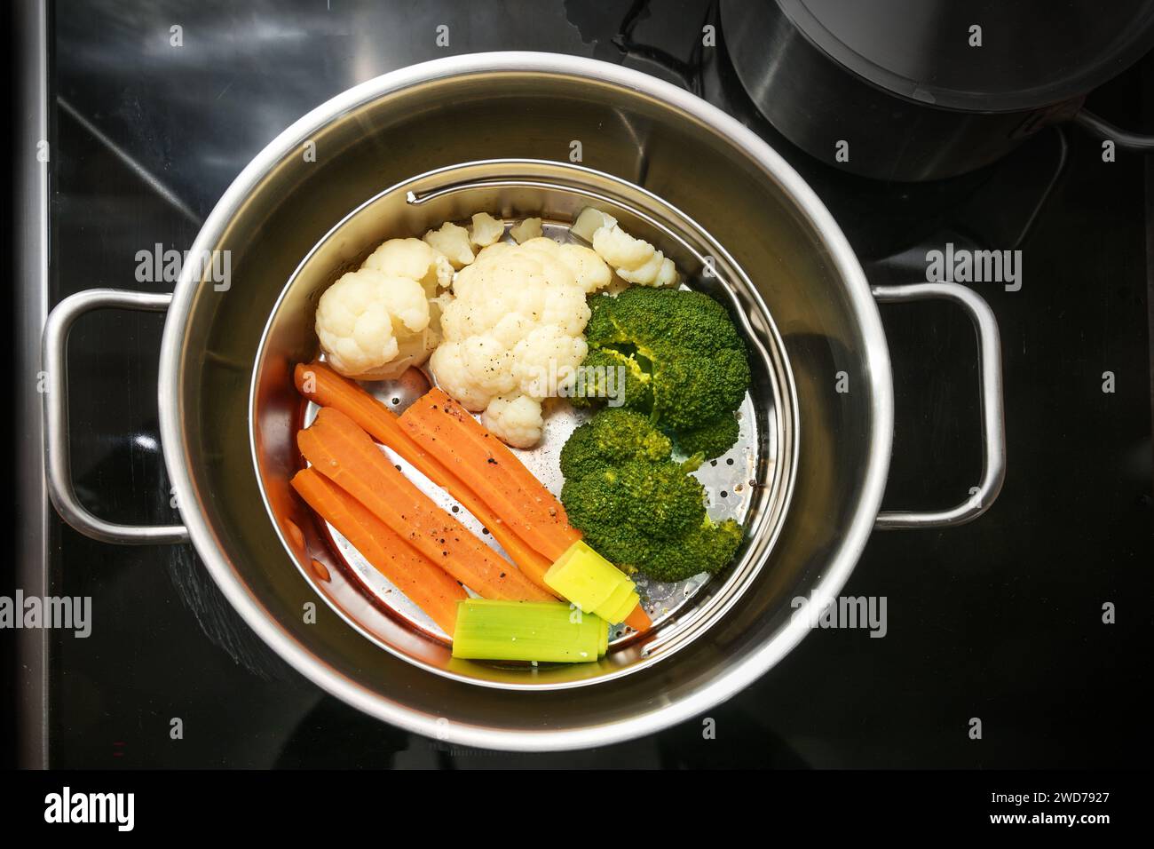 Mezcla de verduras en una cesta de vapor de alimentos en una olla de acero inoxidable, la técnica de cocina saludable que preserva los minerales, vitaminas y sabor, vista superior de Foto de stock