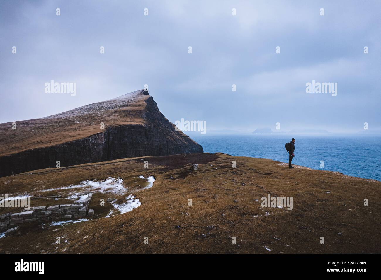 Hombre excursionista se encuentra en el borde del acantilado junto al océano, Islas Feroe Foto de stock
