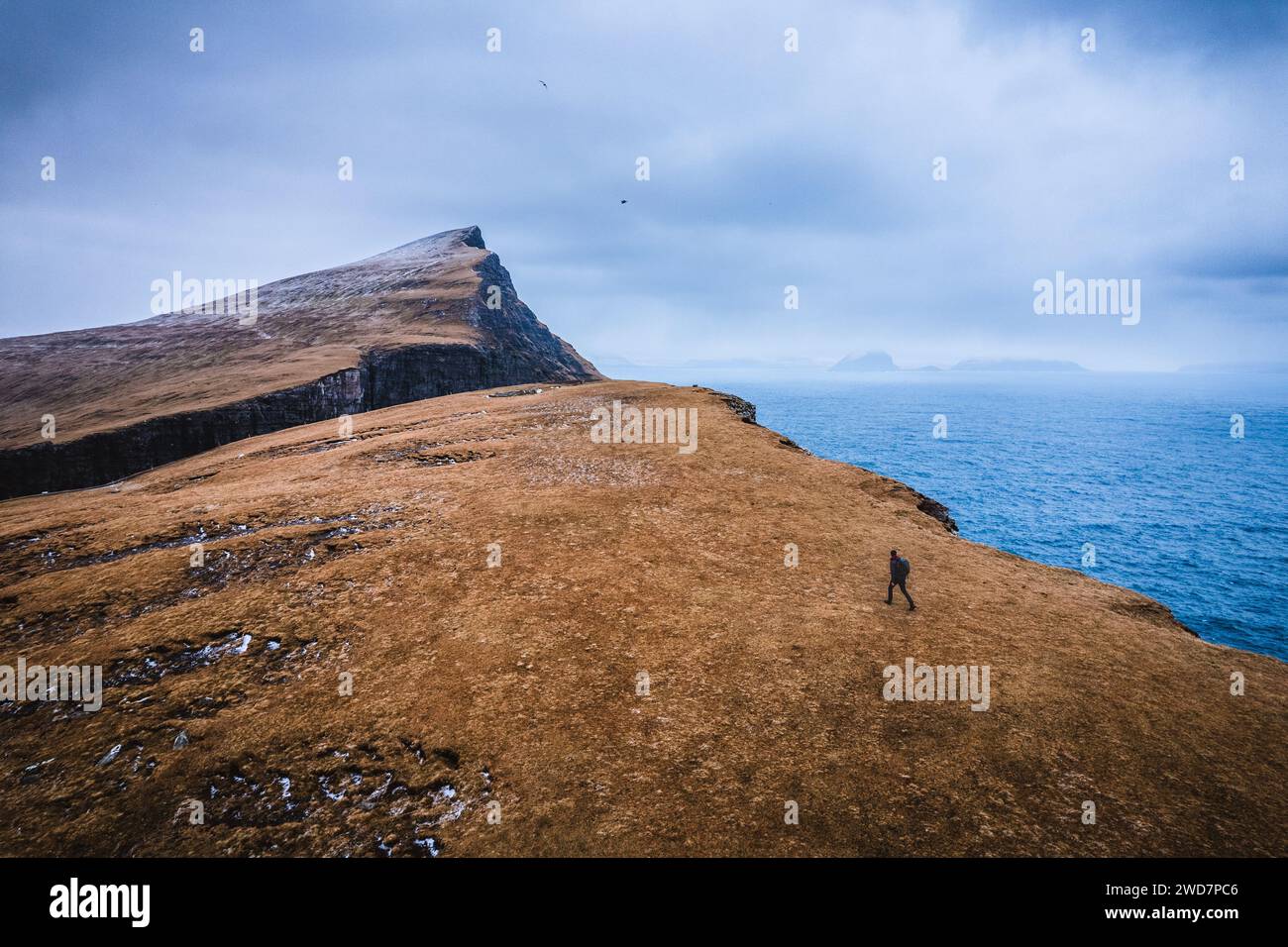 Trekker caminatas a lo largo de la cara del acantilado con montañas dramáticas, Islas Feroe Foto de stock