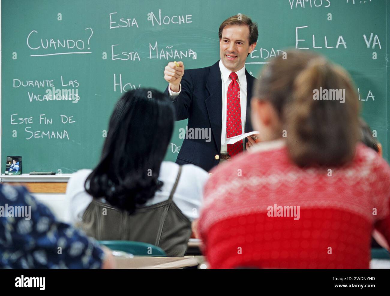 Hombre Caucásico Español Lengua Secundaria Profesor de pie frente a una pizarra con español escrito en el tablero bien cuestionando a sus estudiantes Foto de stock