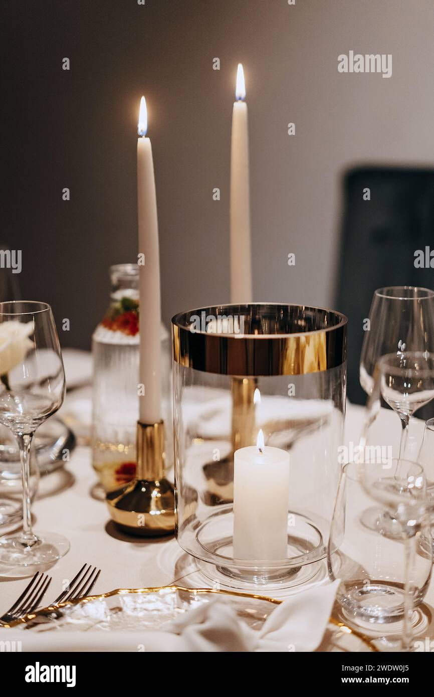 Una mesa de cena adornada con velas encendidas y cristalería elegante Foto de stock