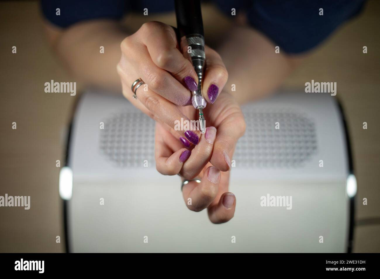 Detalle de la hembra irreconocible quitando su propio esmalte de uñas con lima eléctrica sobre un colector de polvo, DIY manicura de cerca Foto de stock