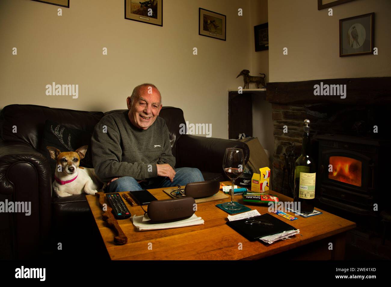 Anciano sentado en su sala de estar con su perro mascota Foto de stock