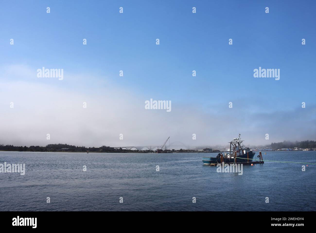 La imagen del paisaje muestra un barco anclado en la bahía de Yaquina, Newport, Oregón. El cielo azul se asoma de las nubes y la niebla. Foto de stock