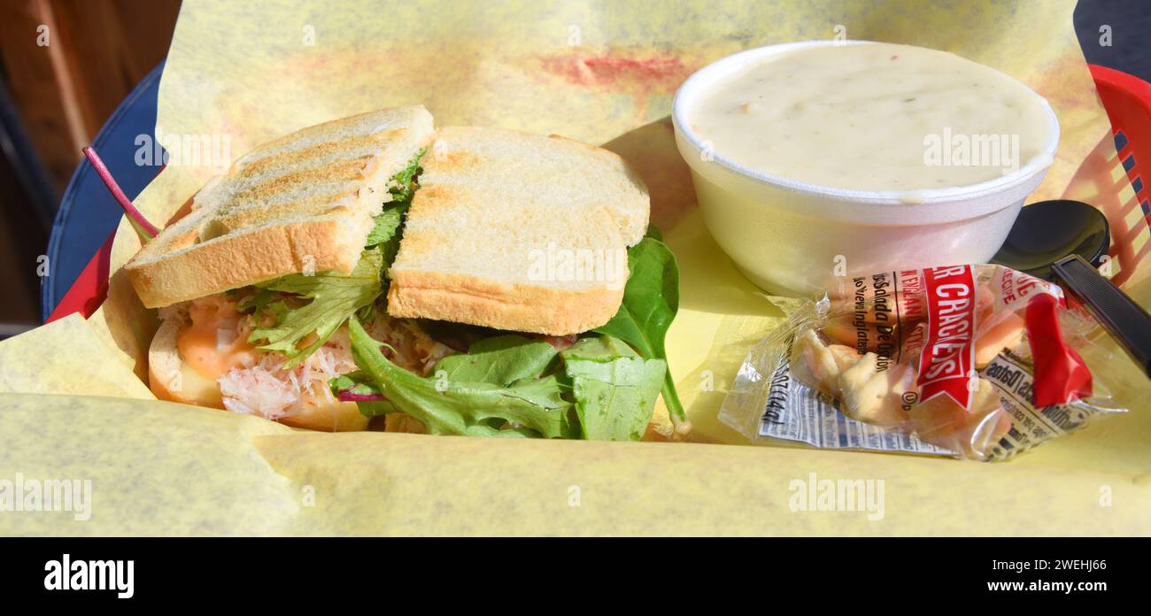 Cesta, con papel amarillo, sostiene un sándwich de cangrejo fresco y un tazón de sopa de almejas. Foto de stock