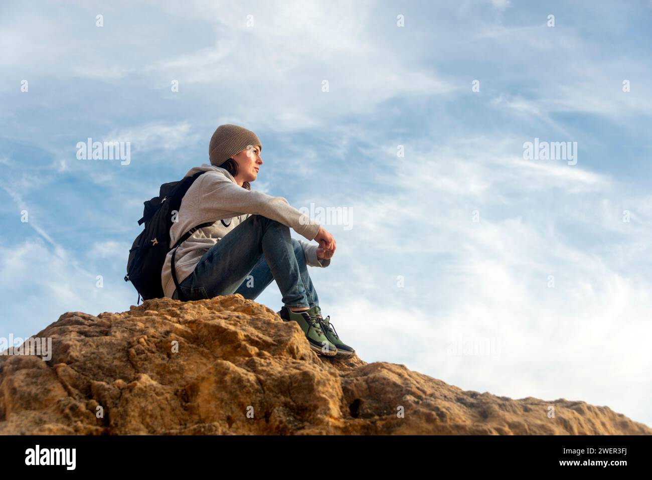 mujer excursionista sentada en la parte superior de una roca mirando la vista Foto de stock
