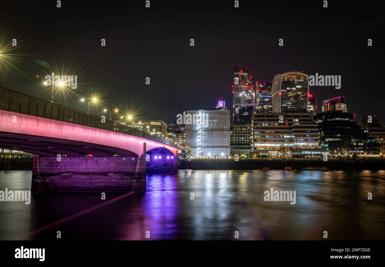 Londres. UK-01.27.2024. Puente de Londres por la noche con el rascacielos en la ciudad de Londres en el fondo y reflejos de luz sobre el río Támesis. Foto de stock
