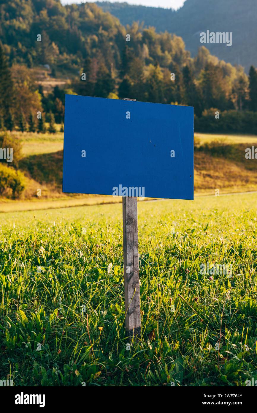 Mockup de madera del cartel de la información azul en prado alpino escénico en la mañana, enfoque selectivo Foto de stock