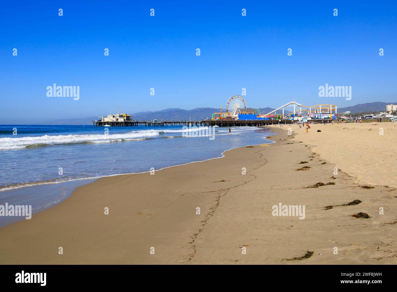 Vista a lo largo de la playa de Santa Mónica hacia el muelle y la montaña rusa Pacific Park y la gran rueda. Santa Mónica, California, Estados Unidos de América. ESTADOS UNIDOS. Foto de stock