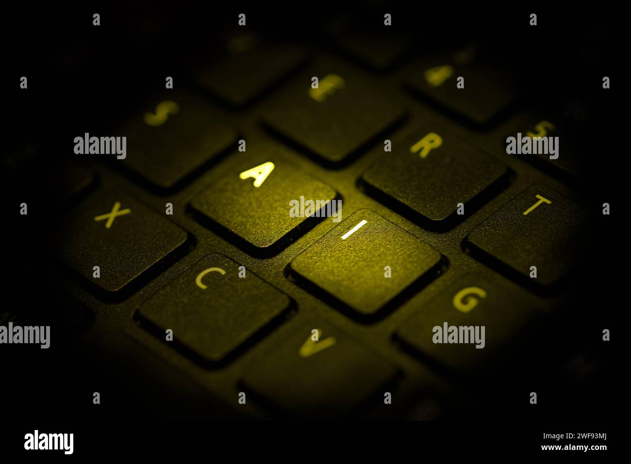 teclado iluminado con luz amarilla resaltando letras a i, de cerca Foto de stock