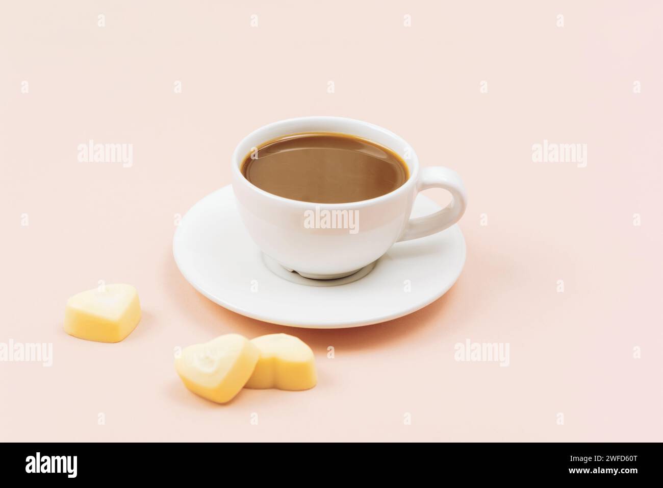 Café en taza blanca y caramelos de chocolate blanco en forma de corazón sobre fondo rosa claro. Concepto del día de San Valentín. En primer plano. Foto de stock