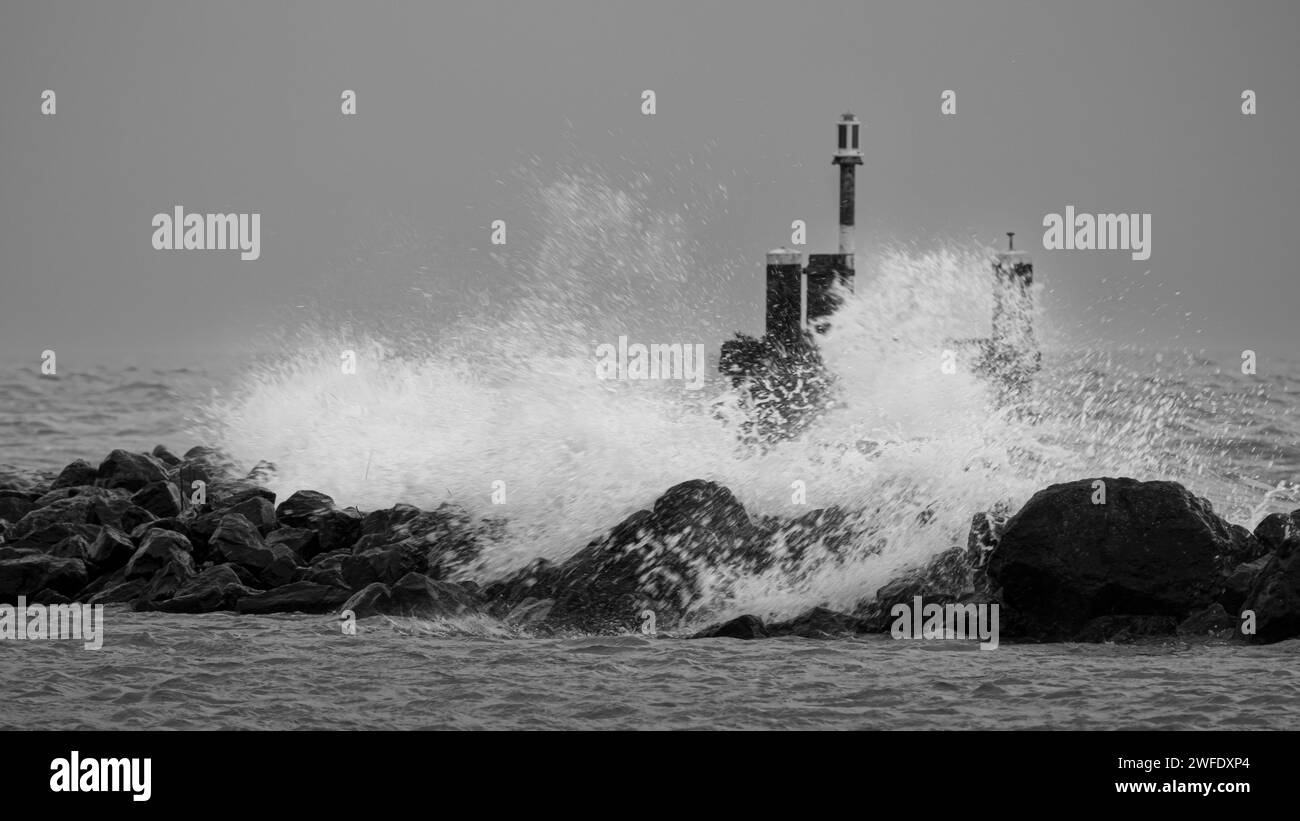 El muelle de piedra soporta fuertes vientos y altas olas del Markermeer. El viento hace que las olas altas choquen contra el malecón de piedra y los delfines. Foto de stock