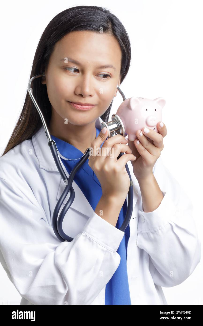Médico asiático americano que examina una alcancía, concepto muestra el alto costo de la atención médica aislada en un fondo blanco con espacio de copia Foto de stock