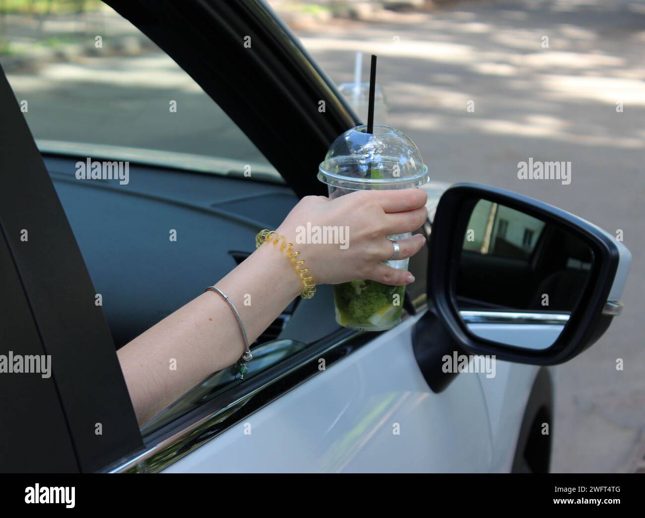 Concepto de conducción ebria. Una mujer puso su mano con un cóctel fuera de la ventana abierta del coche Foto de stock
