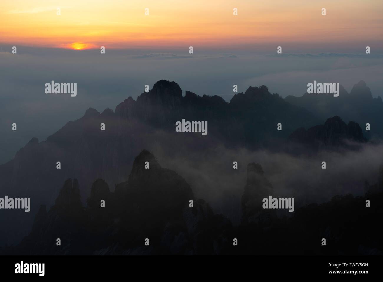 Un sol dorado se pone sobre el Mar de Nubes visto desde Turtle Peak en las Montañas Amarillas de Huangshan. Foto de stock