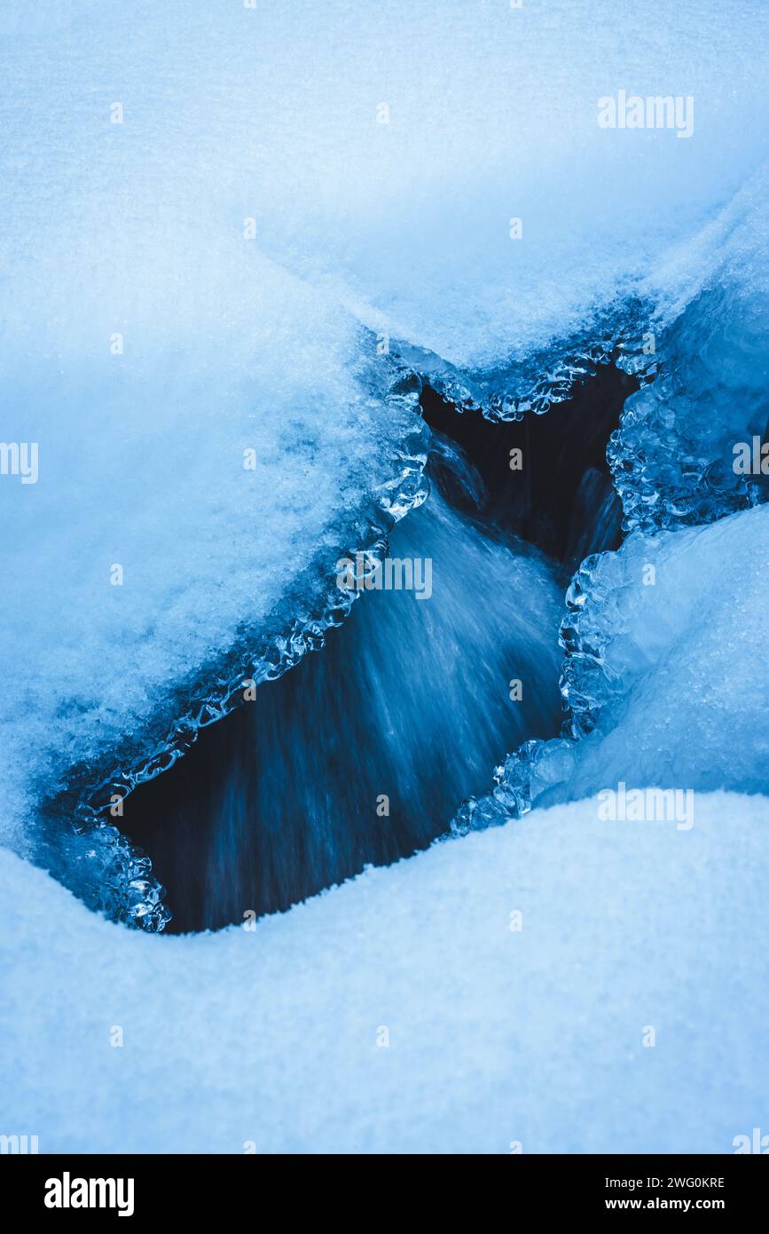 agua corriente de un arroyo justo debajo de un agujero en el hielo Foto de stock