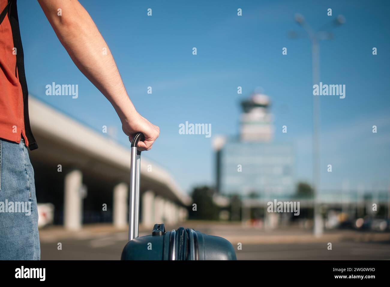 Viaje en avión. El viajero está caminando desde el estacionamiento hasta la terminal del aeropuerto. Hombre con maleta contra la torre de control de tráfico aéreo en el día soleado de verano. Foto de stock