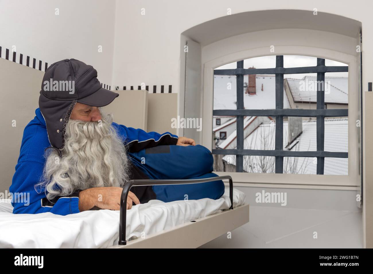 Un hombre triste con barba está acostado en una litera en una celda de la prisión Foto de stock