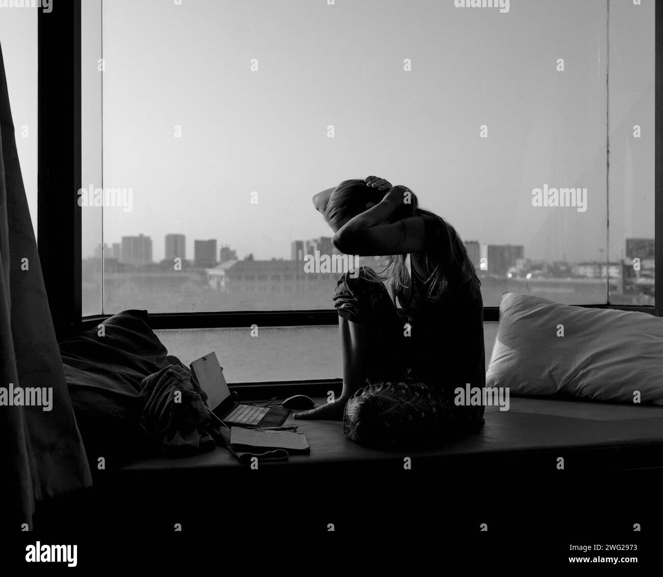 Una chica se sienta sola en una ventana. Foto de stock