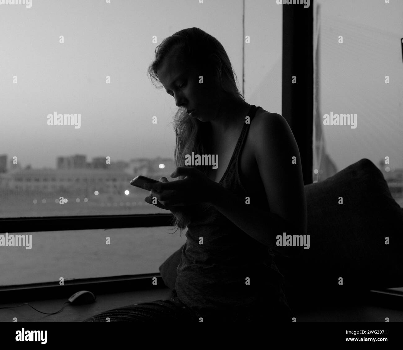 Una chica se sienta sola en una ventana. Foto de stock